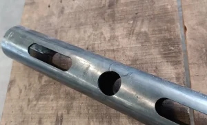 Un primer plano de una varilla de metal con múltiples agujeros perforados, colocada sobre una superficie de madera.