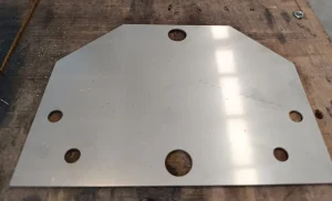 Una placa de metal con cinco agujeros circulares dispuestos en forma semihexagonal, situada sobre una superficie de madera.