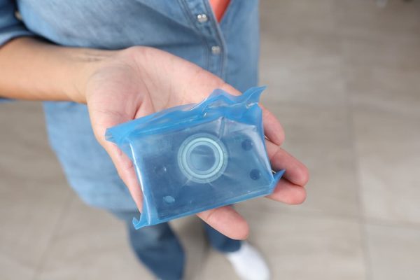 Una persona con una camisa vaquera sostiene un paquete azul sellado que contiene un rodamiento de metal.