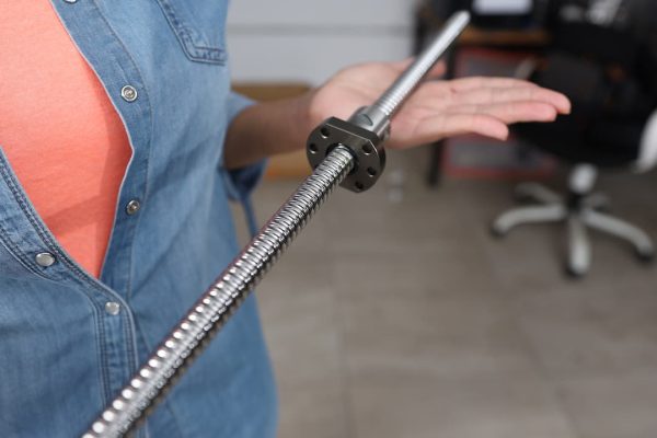 Persona que sostiene una varilla de tornillo de metal larga en su mano, vistiendo una camisa vaquera.