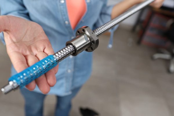 Persona sosteniendo un tornillo de metal con una tuerca de bronce y un mango azul, mostrándolo a la cámara.