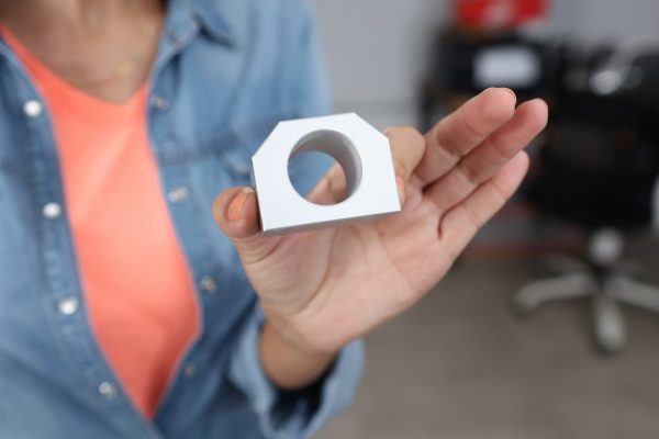 Una persona sostiene un objeto metálico pequeño y rectangular con un agujero circular en el centro.