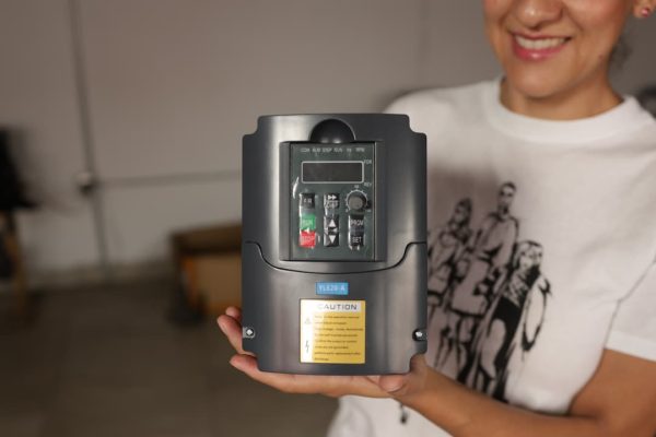 Persona que sostiene un dispositivo electrónico negro con pantalla y botones, etiquetado con una pegatina de precaución.