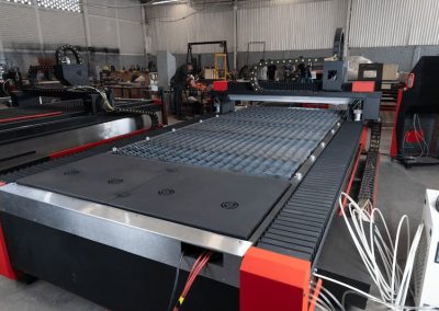 Gran máquina CNC industrial en un taller con componentes metálicos y electrónicos visibles. La máquina está rodeada de otros equipos y herramientas.