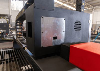 La maquinaria industrial con un componente rojo está situada en un espacioso taller, que cuenta con un panel de metal y ventilación.