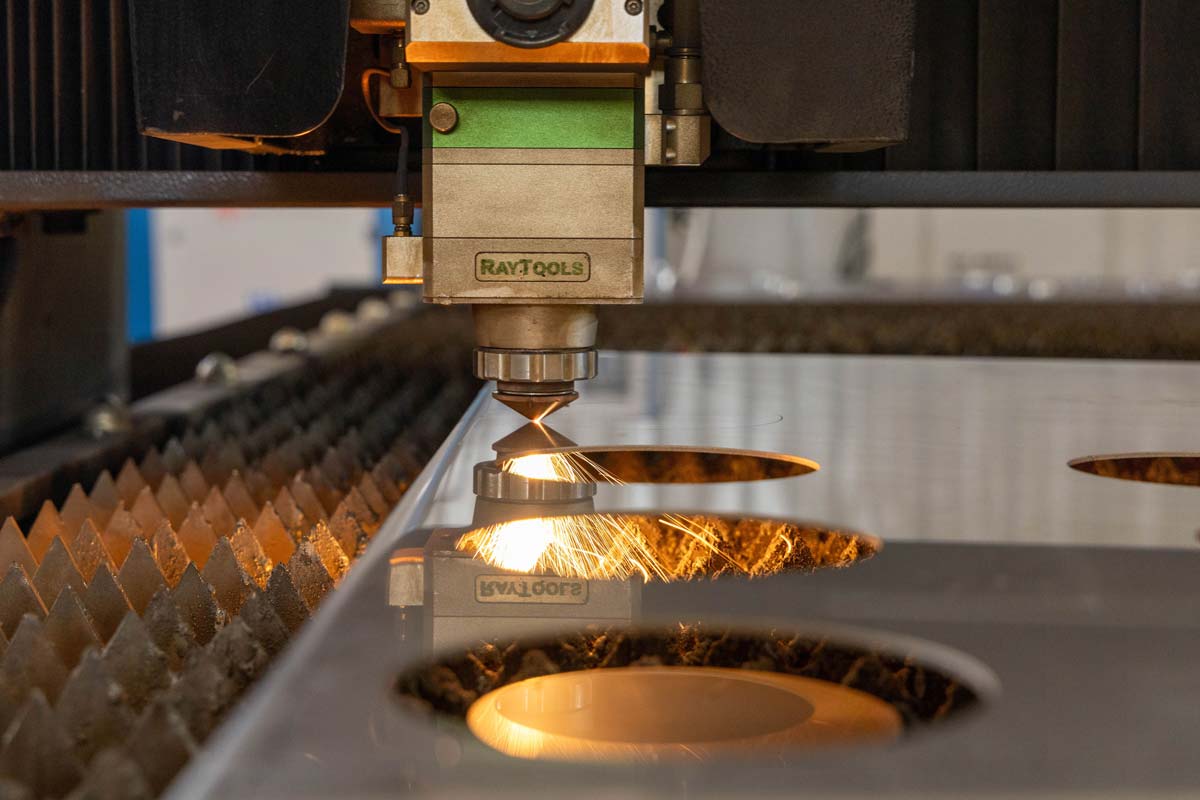 Una máquina de corte láser CNC corta con precisión formas circulares en una lámina de metal, con chispas visibles en el punto de corte del láser.