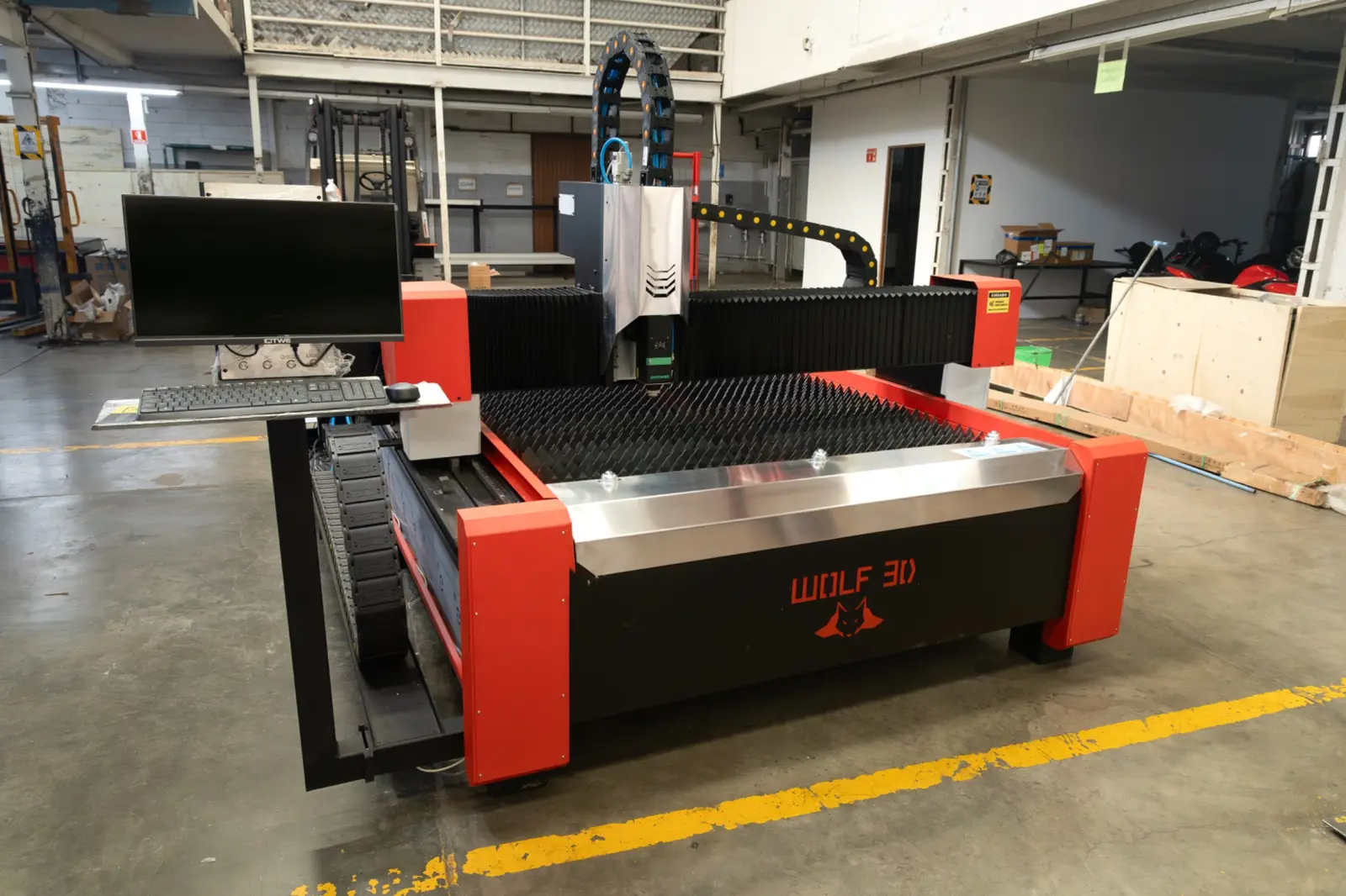En el espacio de trabajo de un almacén se encuentra una máquina CNC industrial WOLF 3D de color rojo y negro, equipada con un monitor de ordenador.