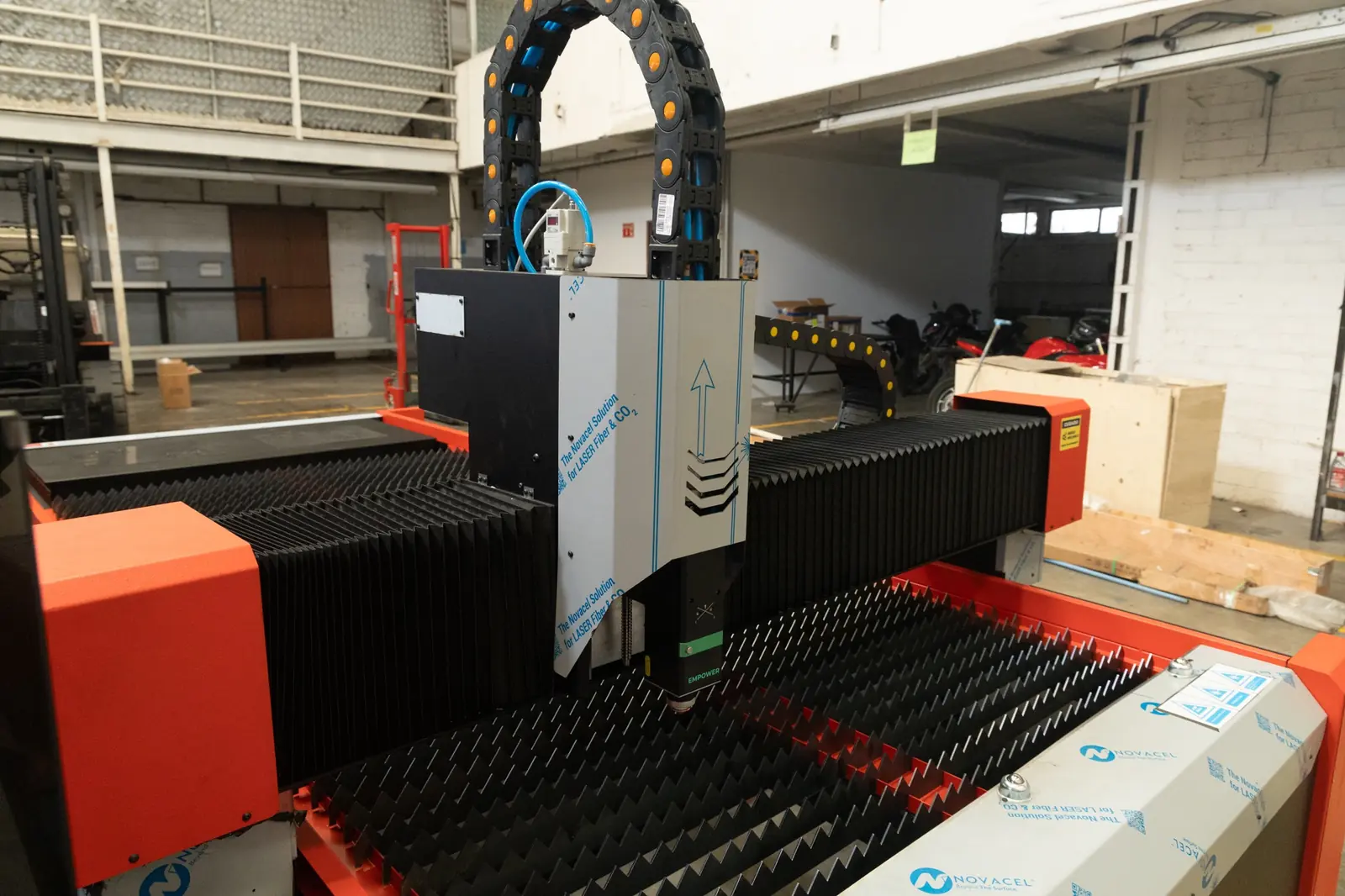 Una máquina de corte por láser CNC con un cabezal de corte de metal está situada sobre una mesa de trabajo con púas en un espacio de trabajo industrial.