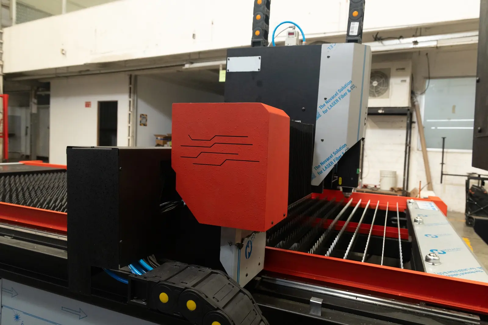 Un primer plano del cabezal de una máquina CNC, con componentes negros y rojos, en el que se aprecian los rieles metálicos y la mesa de trabajo, en el entorno de un taller industrial.