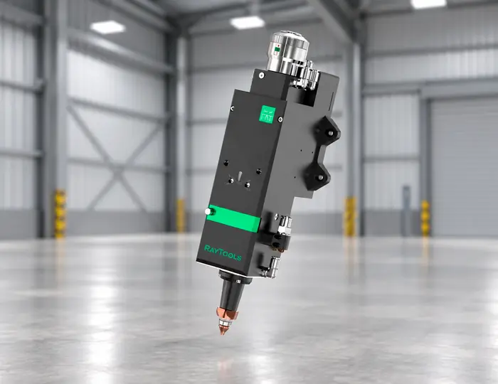 Un cabezal de corte por láser industrial de Raytools está suspendido en un gran almacén vacío, con paredes grises y suelo de hormigón pulido.